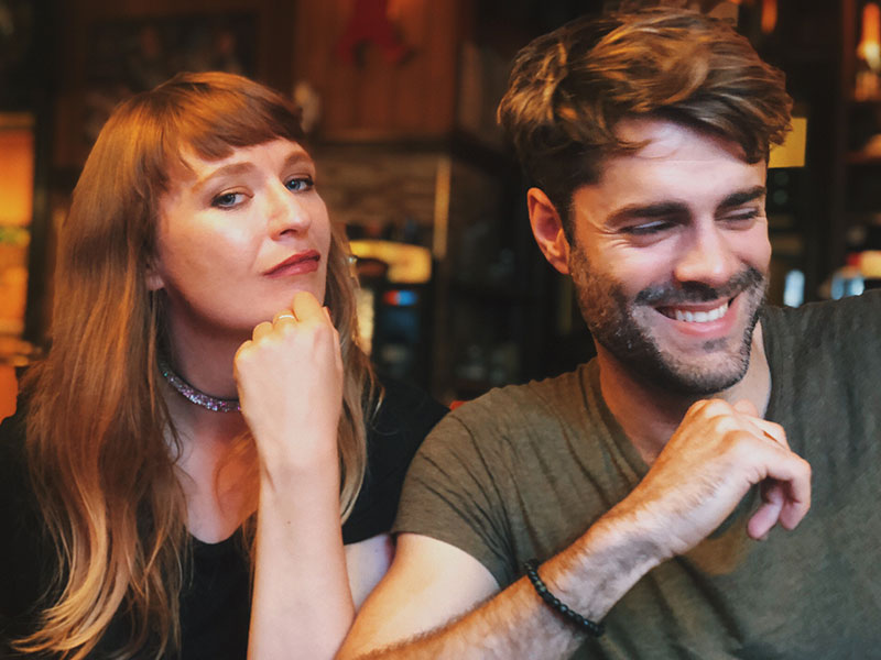 A woman who's feeling jealousy in an open relationship giving her boyfriend a doubtful look while they're at the bar together.