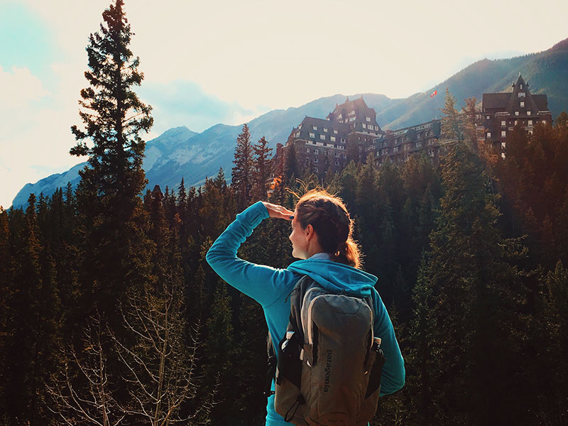 A woman who's surviving infidelity, hiking in the woods and looking towards the sun.