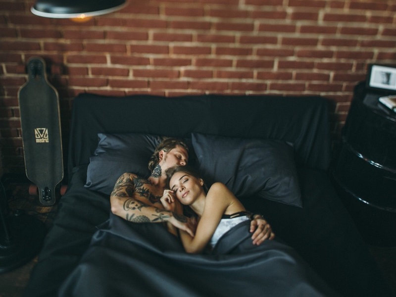 Happy couple lying in each other's arms in bed, enjoying a healthy sex life