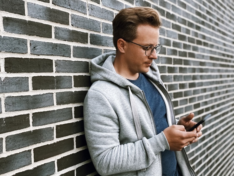 Man leaning against a wall swiping right on dating app on his phone