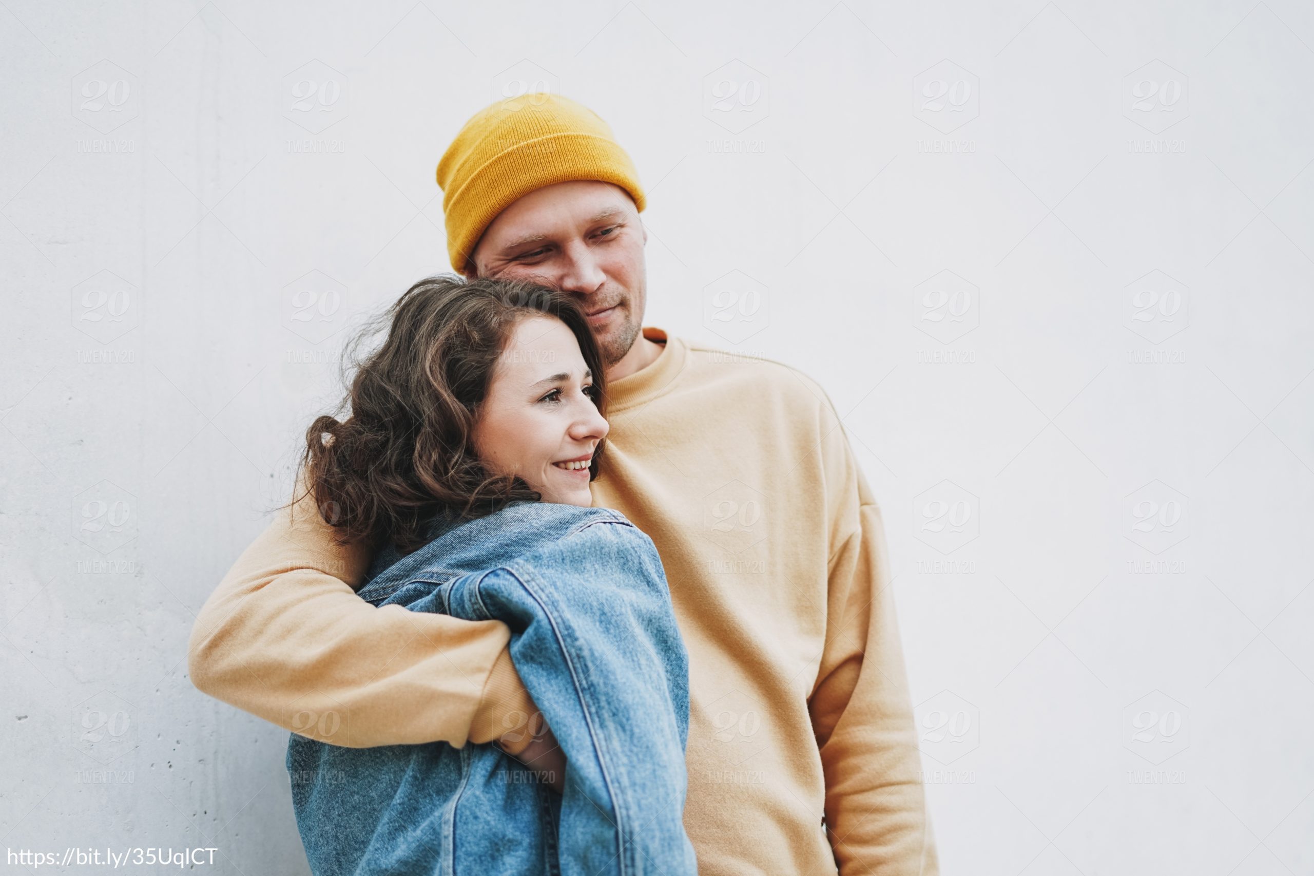 happy couple hugging each other in front of white wall