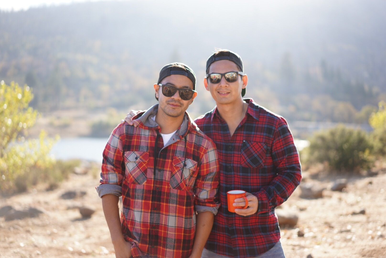attractive gay couple both wearing flannel shirts in the outdoors with their arms around each other