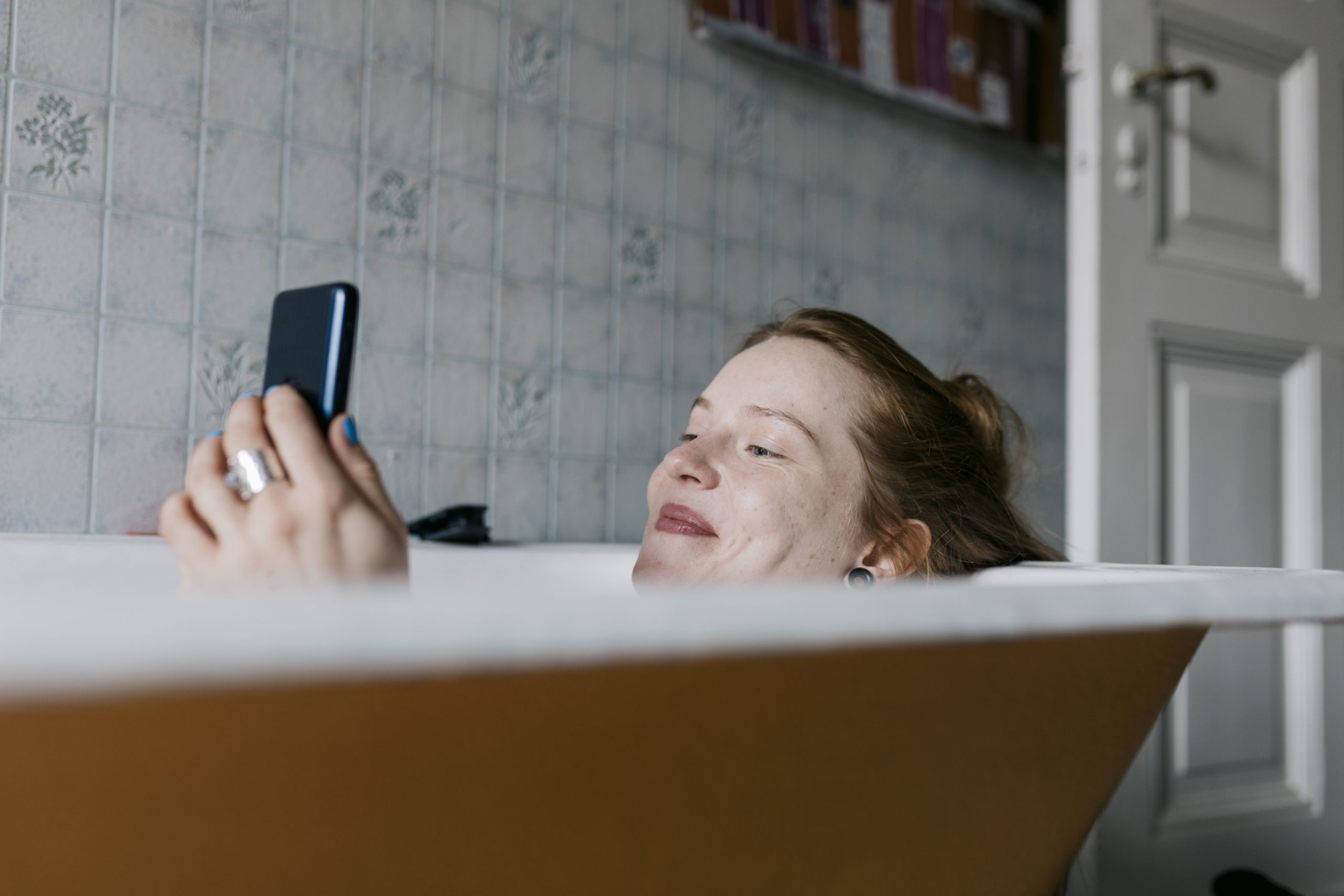 Woman in bath smiling and texting funny response to "what's up" message.