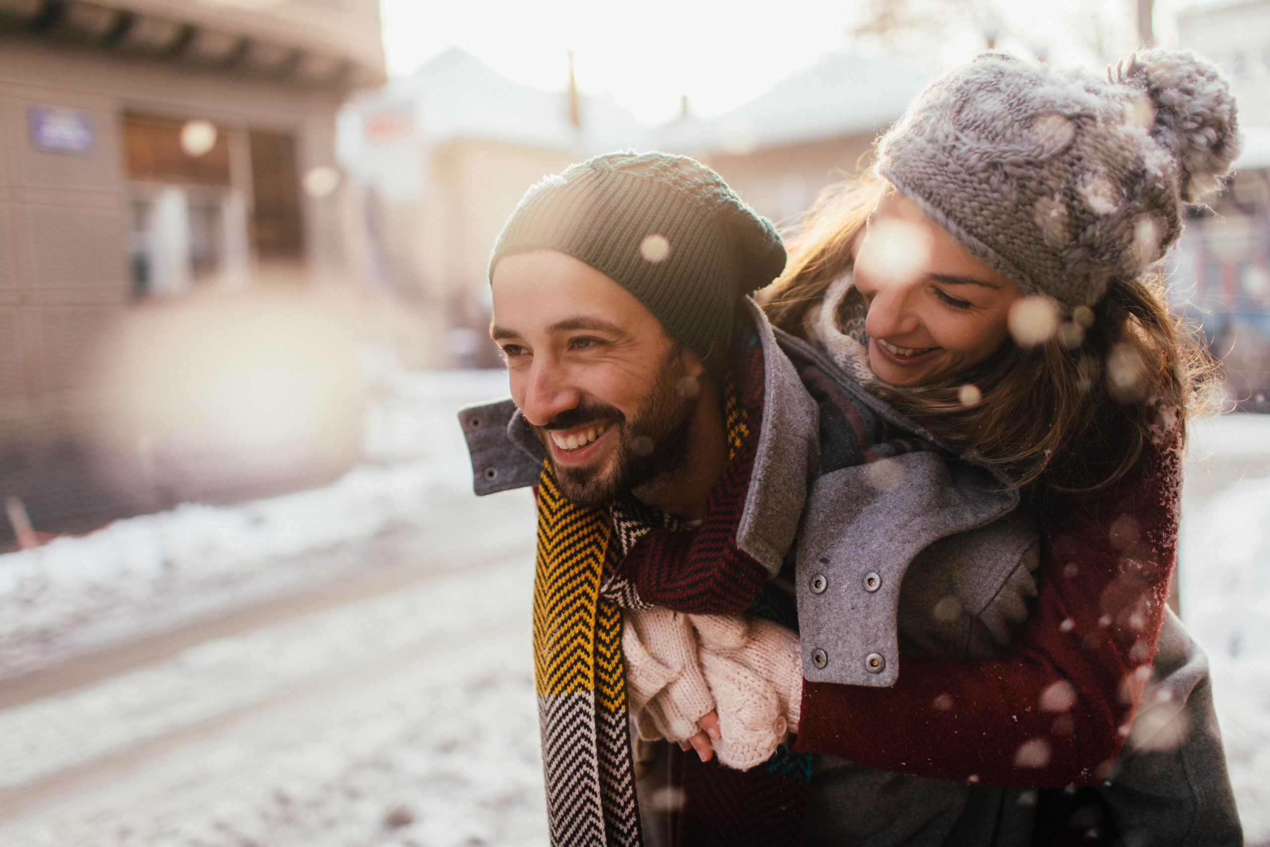 Romantic couple smiling and laughing together on a snowy day while trying out some cute winter date ideas.