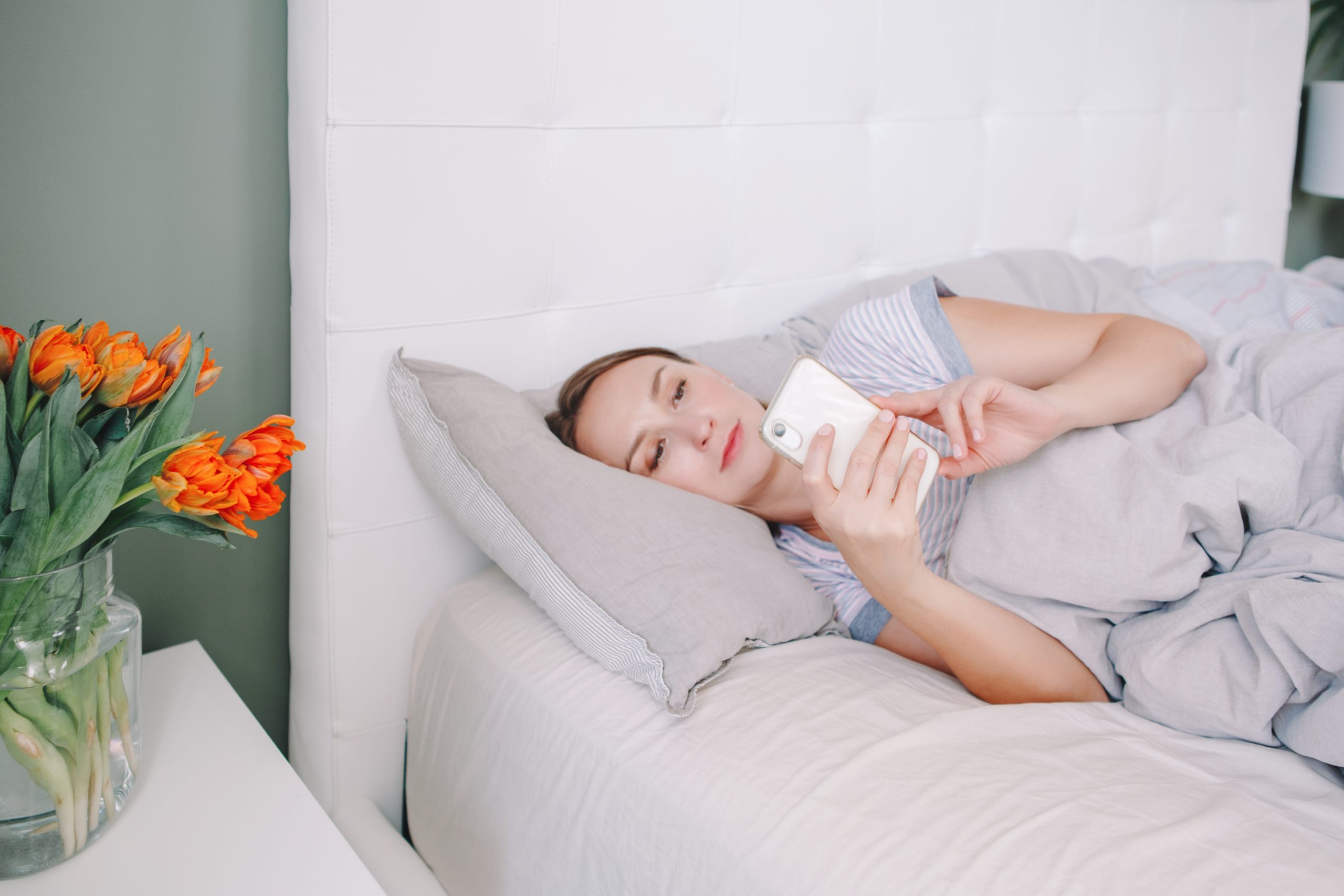 Smiling woman lying in bed on her phone reading a good morning paragraph for her from her partner.