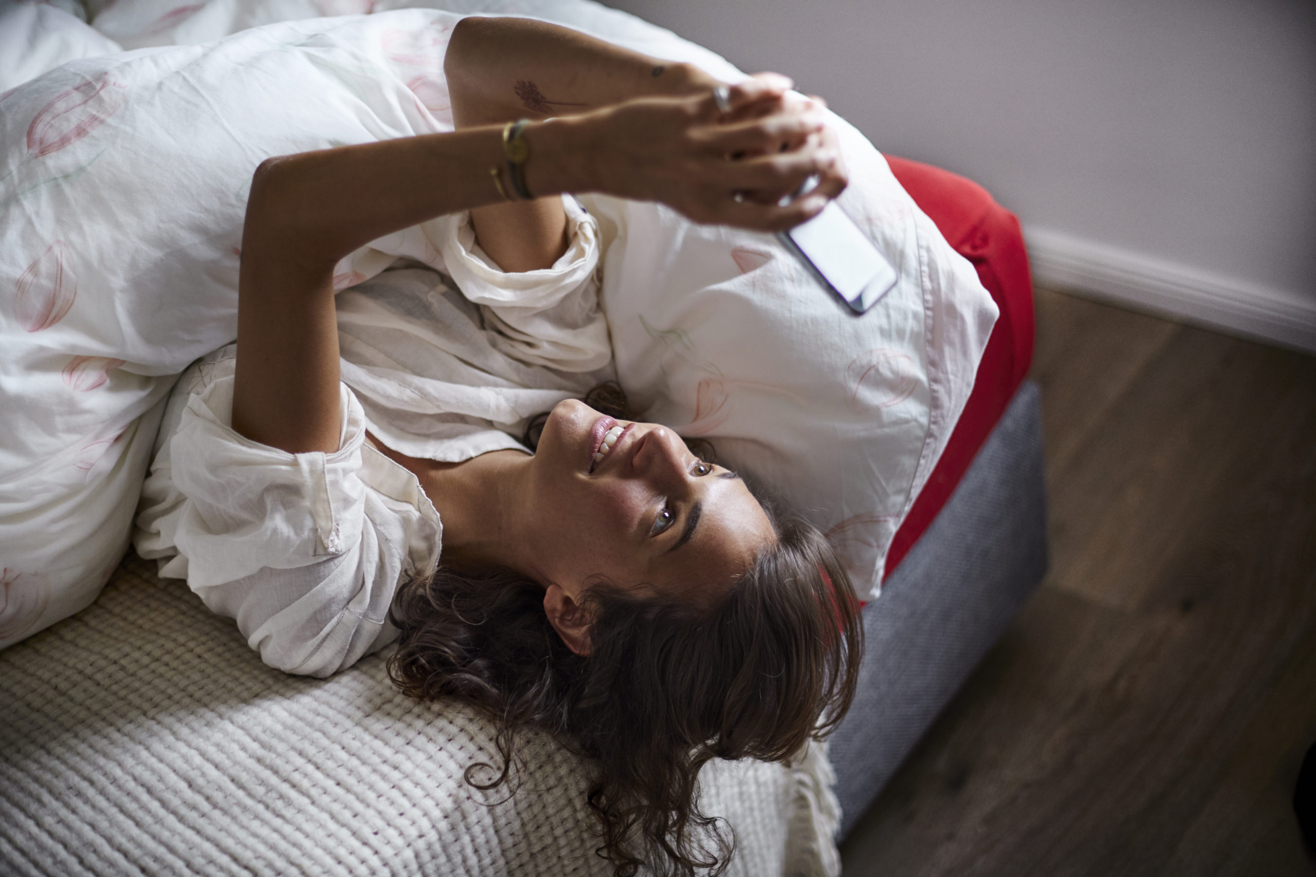 Attractive young woman lying on bed while writing a subtle and seductive text message for him.