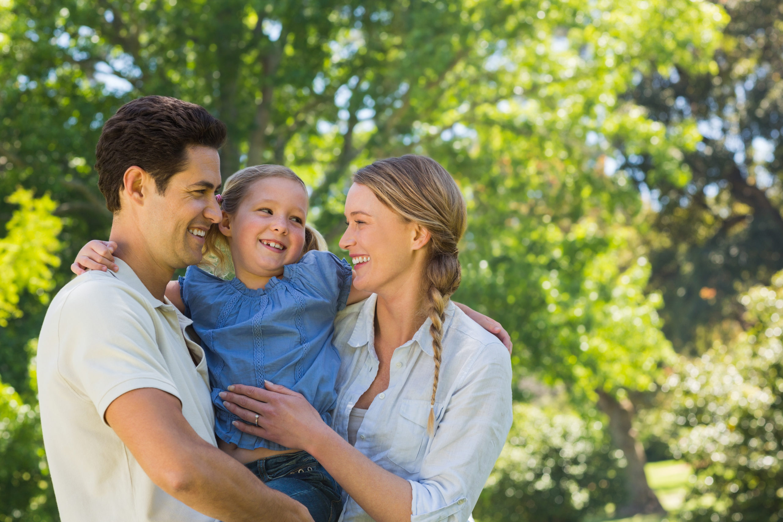 Man dating a single mom and laughing together with her and her daughter in the park on a sunny day,