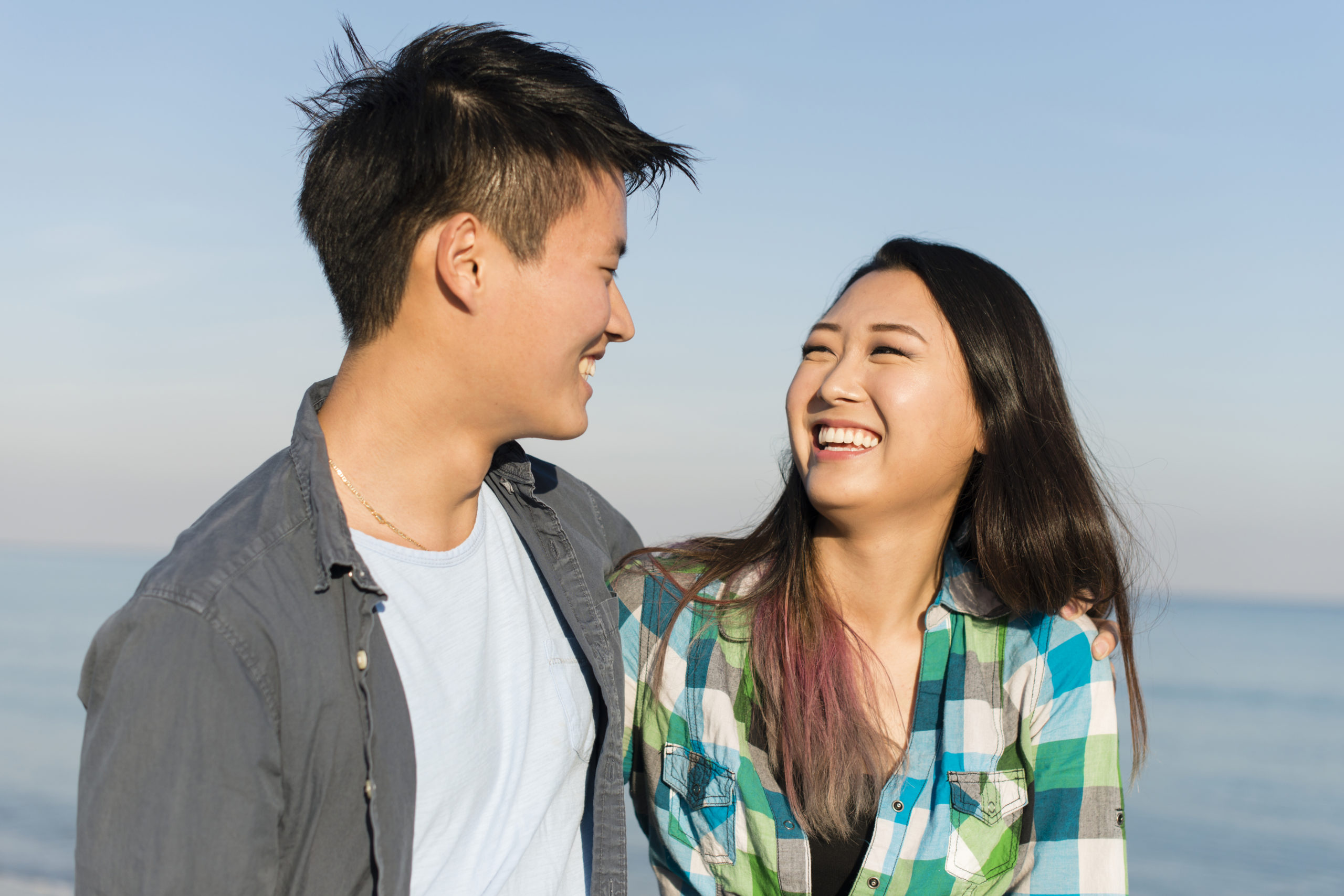 Happy, smiling Asian couple walking in the sunshine and looking into each other's eyes while Korean dating.