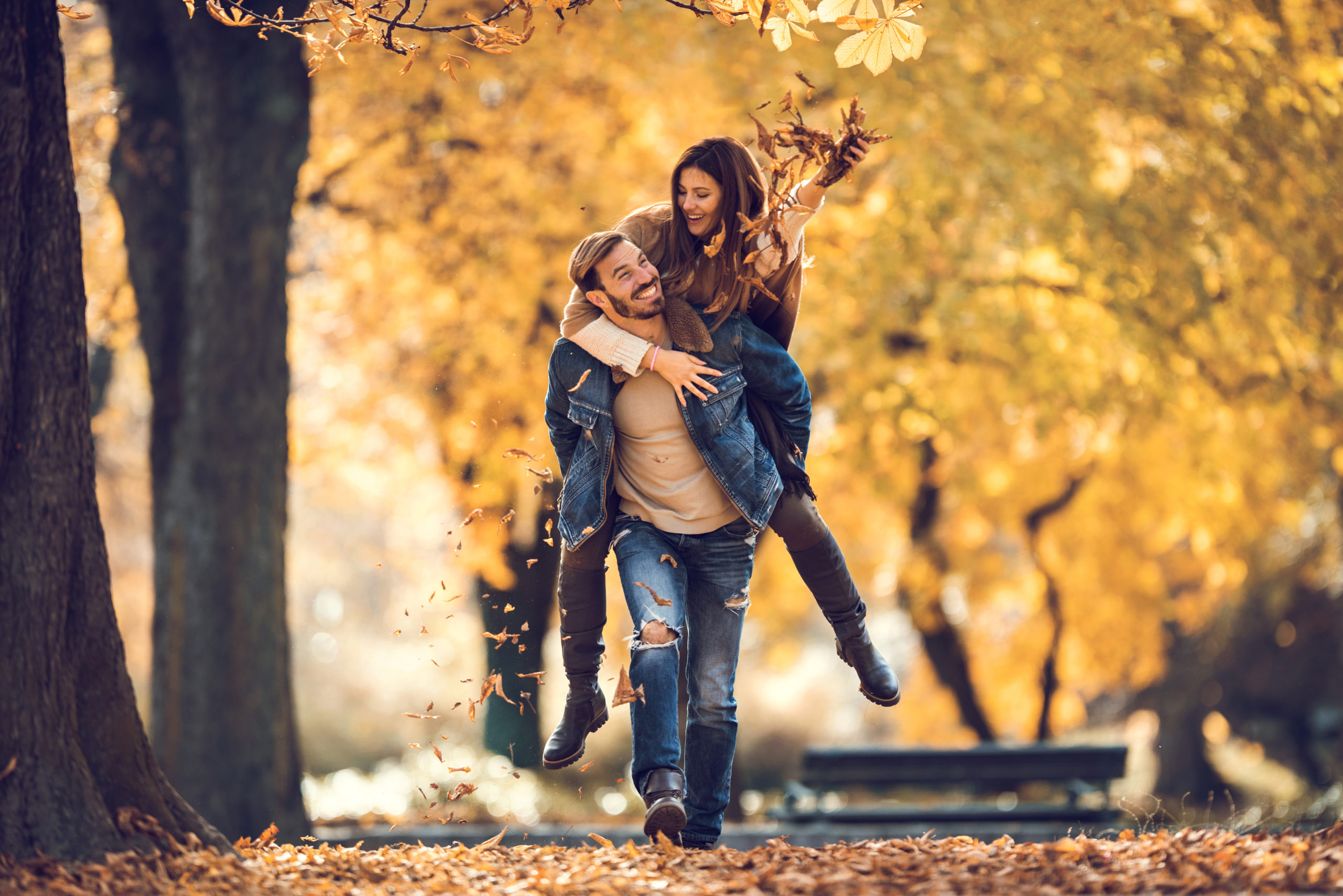 Two Cincinnati singles in autumnal park setting, on a date, with man giving woman a piggy-back.