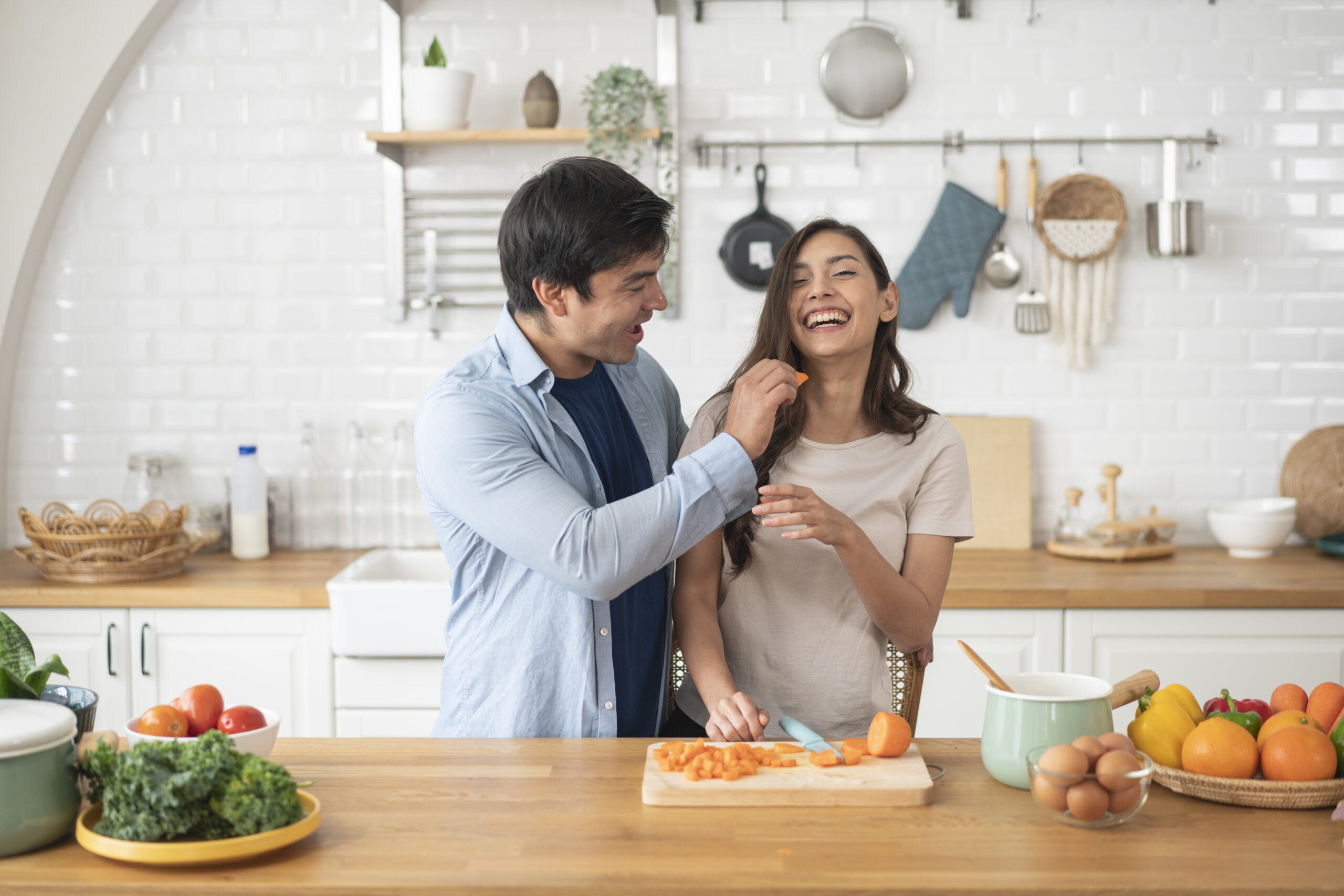 Affectionate couple experiencing vegan dating and standing in a kitchen chopping vegetables for a salad and laughing together..
