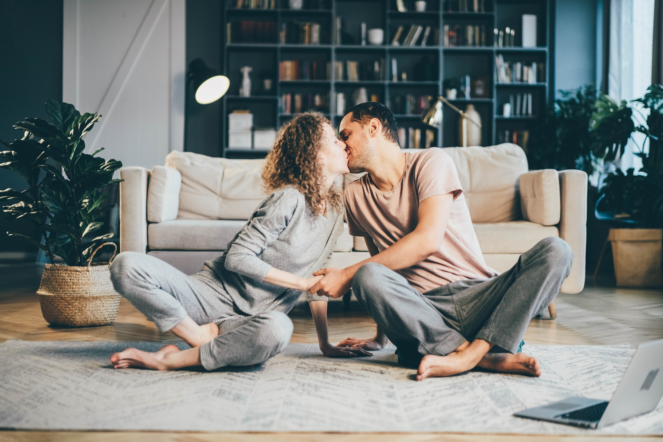 Happy couple sitting on the carpet in their pajamas and kissing after meeting on a spiritual dating app.