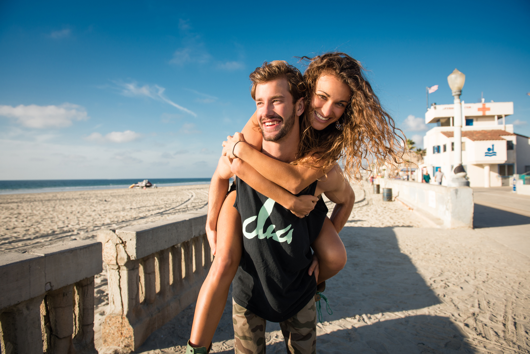 Young man giving girlfriend a piggy back at the beach while enjoying the best date ideas in San Diego.