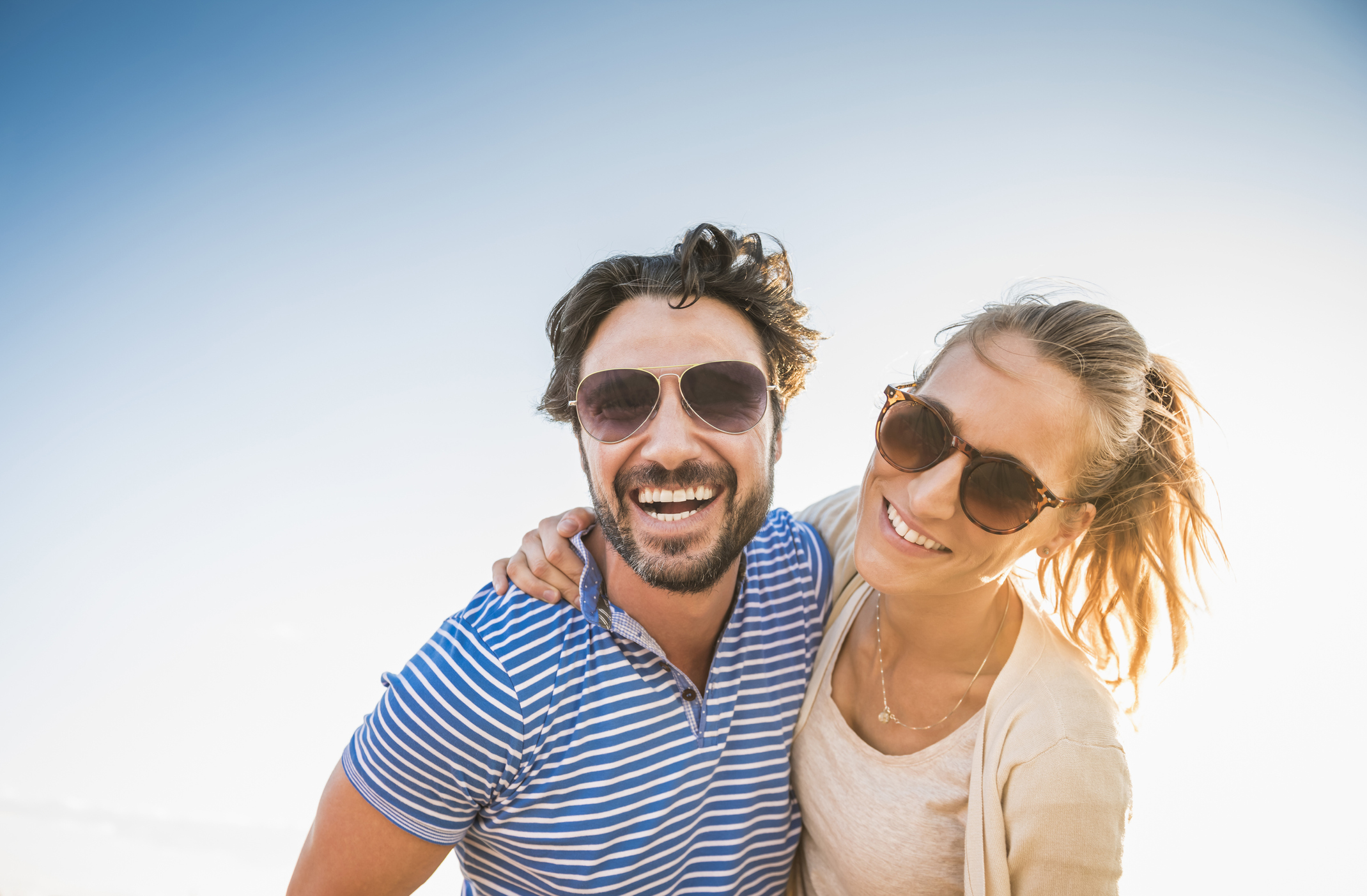 Two young, happy Albuquerque singles looking towards the camera and embracing each other on a sunny day while dating.
