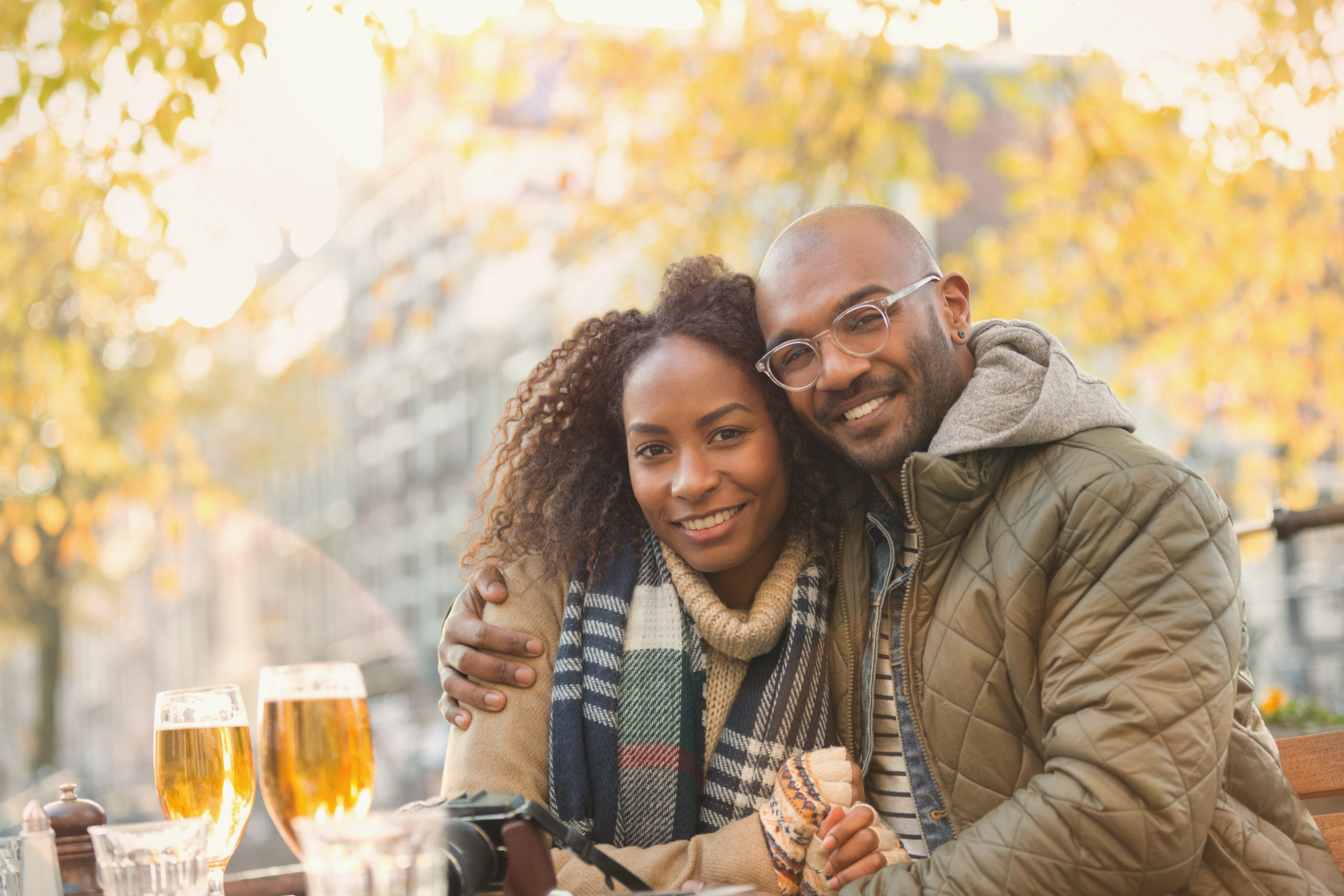 Portrait of a smiling young couple hugging and sitting outdoors in autumnal scene while dating in Baltimore.