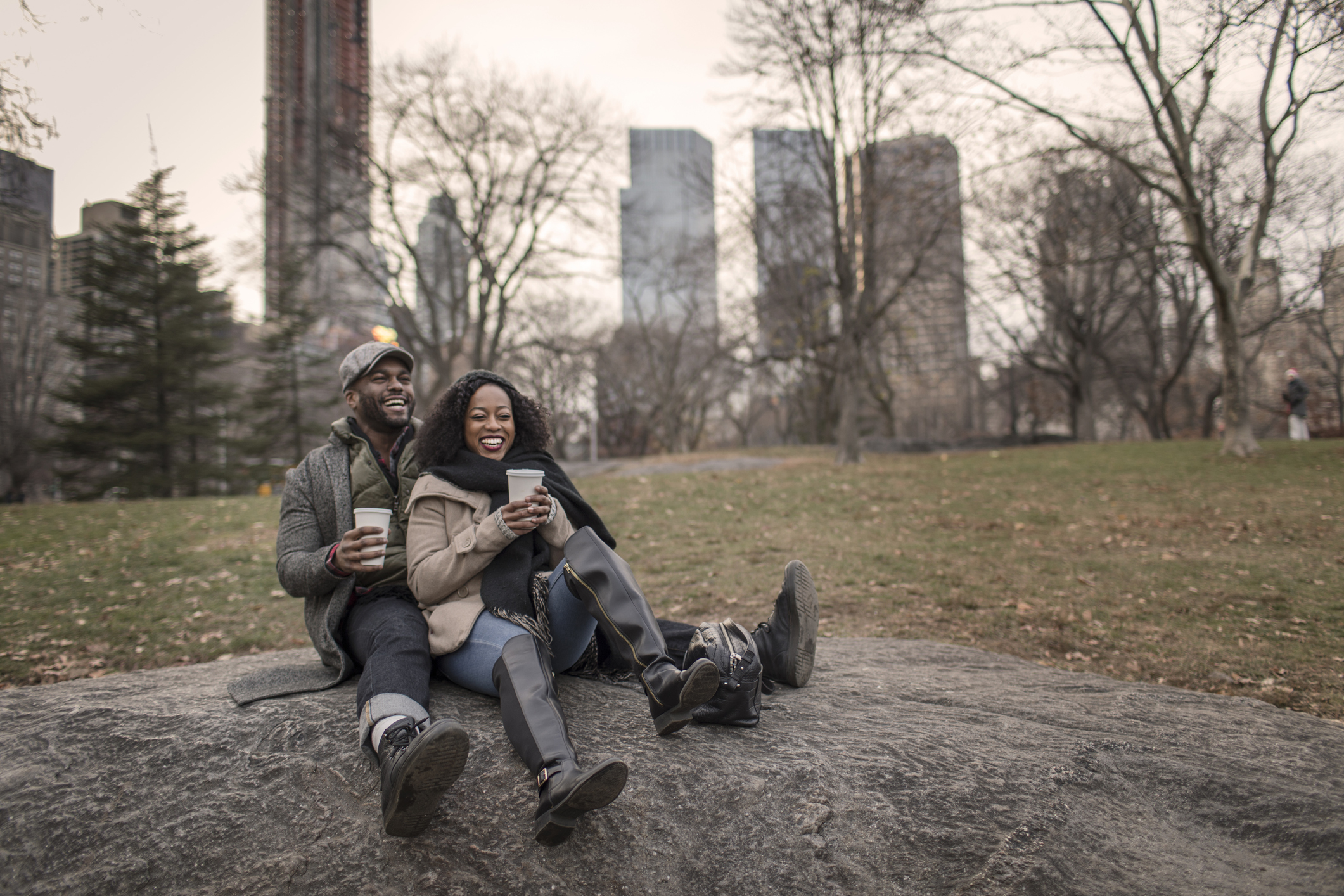 Smiling couple on a date, sitting on a rock outdoors and enjoying one of the most romantic things to do in NYC.